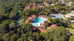 Vista aerea di un resort con piscina, campi da tennis e vegetazione lussureggiante.