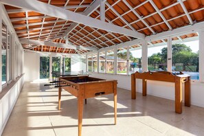 Un espacio interior amplio con mesa de fútbol y mesa de billar, ventanas grandes que ofrecen vistas al exterior y un techo alto con tejas.