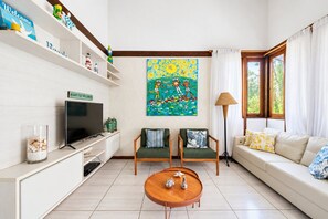 Un salon comprenant un téléviseur, deux fauteuils, un canapé, une table basse et un tableau accroché au mur.