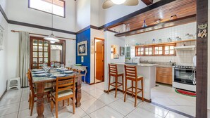 Una sala da pranzo spaziosa con un tavolo di legno apparecchiato per sei persone, una cucina con mobili bianchi e un fornello, e una ventola a soffitto.