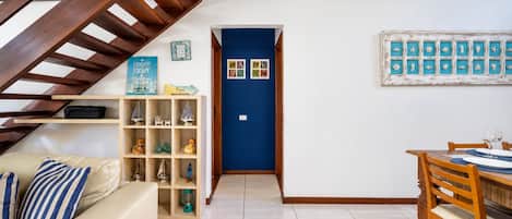A room with a wooden staircase, a blue door, a dining table with chairs, and a shelf with decorative items.