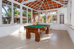 Un grand espace intérieur abritant une table de billard, avec de grandes fenêtres et un plafond en bois.