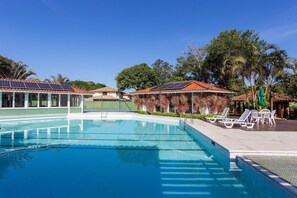 A swimming pool with lounge chairs and a covered area with solar panels. - Bz49 Casa 350m da praia Condomínio (Buzios)