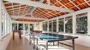 Un'area ricreativa interna con tavolo da ping pong, una panca di legno e ampie finestre che offrono vista sull'esterno.