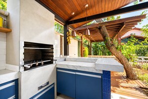 An outdoor kitchen with a built-in grill, blue cabinets, and a wooden pergola overhead. - Bz49 Casa 350m da praia Condomínio (Buzios)