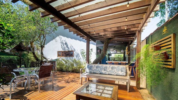 Una terrazza in legno con un tavolo dal piano in vetro, sedie bianche e una panca con cuscino blu.