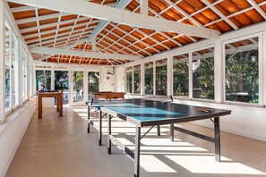 Un espace de loisirs intérieur comprenant une table de ping-pong, un banc en bois et de grandes fenêtres donnant sur l’extérieur.