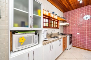 A kitchen with white cabinets, a microwave, a sink, and a clock on the wall. - Bz49 Casa 350m da praia Condomínio (Buzios)