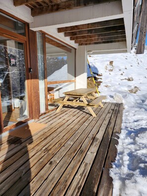 A wooden deck with a table and chairs, a glass door, and a snowy landscape in the background.