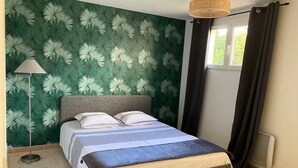 A bedroom with a bed, a floor lamp, a window with curtains, and a wall with a leafy pattern. - Mountain views with Heated pool and optional Jacuzzi. South of France (Olargues)