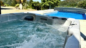 A hot tub with a pool in the background, surrounded by greenery and a clear sky. - Mountain views with Heated pool and optional Jacuzzi. South of France (Olargues)