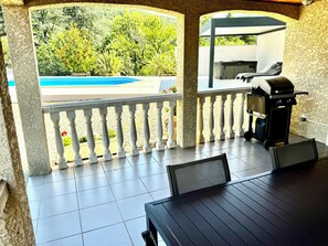 An outdoor patio with a pool view, a grill, and a table with chairs.