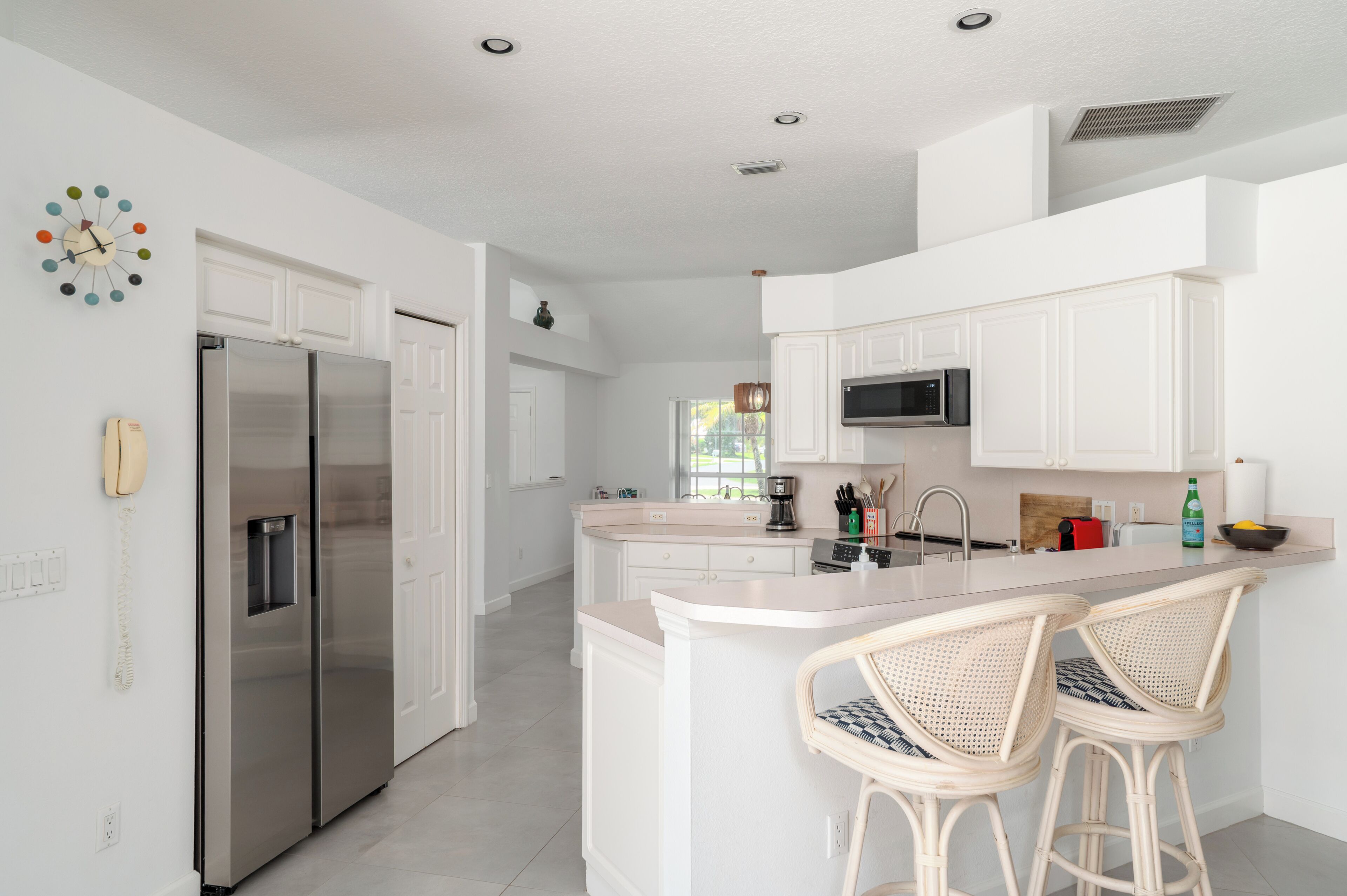 A modern kitchen with white cabinetry, stainless steel appliances, and a central island with bar stools.