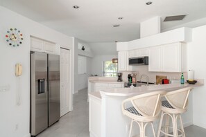A modern kitchen with white cabinetry, stainless steel appliances, and a central island with bar stools.