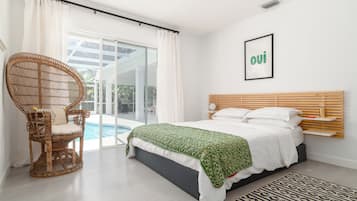 A bedroom with a bed, a wicker chair, a pool view, and a 'oui' sign on the wall.