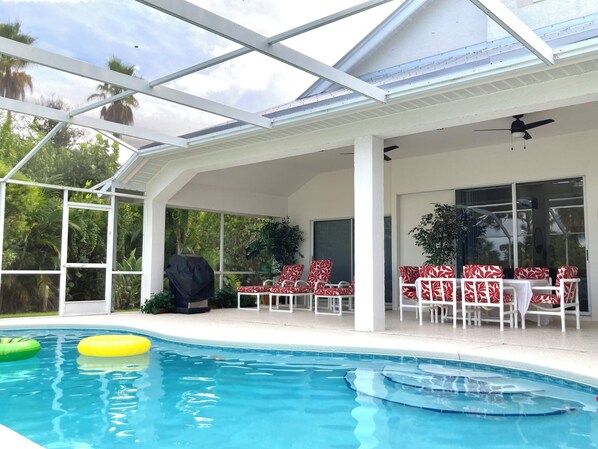 Ein überdachter Poolbereich mit Glasdach, roten und weißen Sitzmöbeln und einem Deckenventilator.