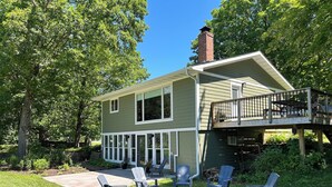 A two-story house with a deck, outdoor seating area with Adirondack chairs, and a chimney.