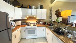 Una cocina compacta con armarios blancos, estufa, pileta y refrigerador.