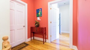 Un pasillo con piso de madera, pared roja y puerta blanca.