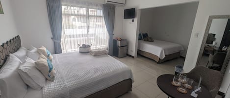 A hotel room with a large bed, a smaller bed, a desk with a chair, a TV, and a window with curtains.