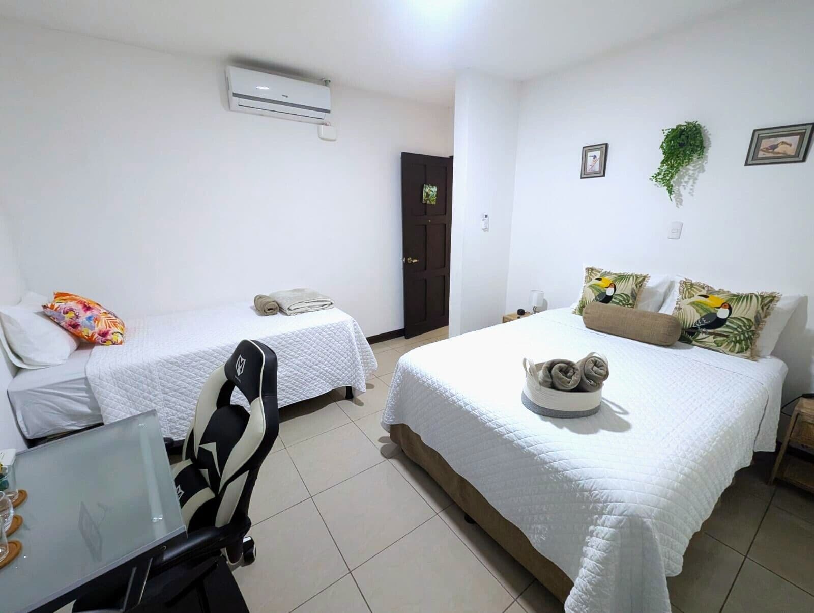 Habitación de hotel con dos camas individuales, un escritorio con silla, aire acondicionado y una puerta.