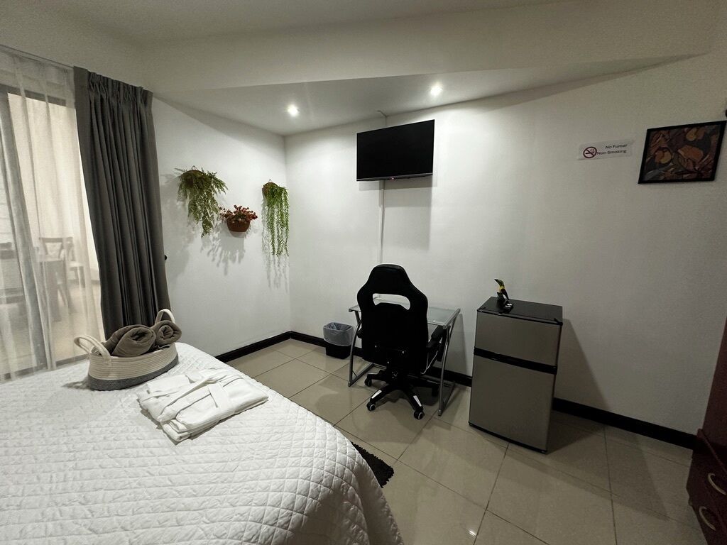 A hotel room with a bed, a desk, a chair, a TV, and a small refrigerator.
