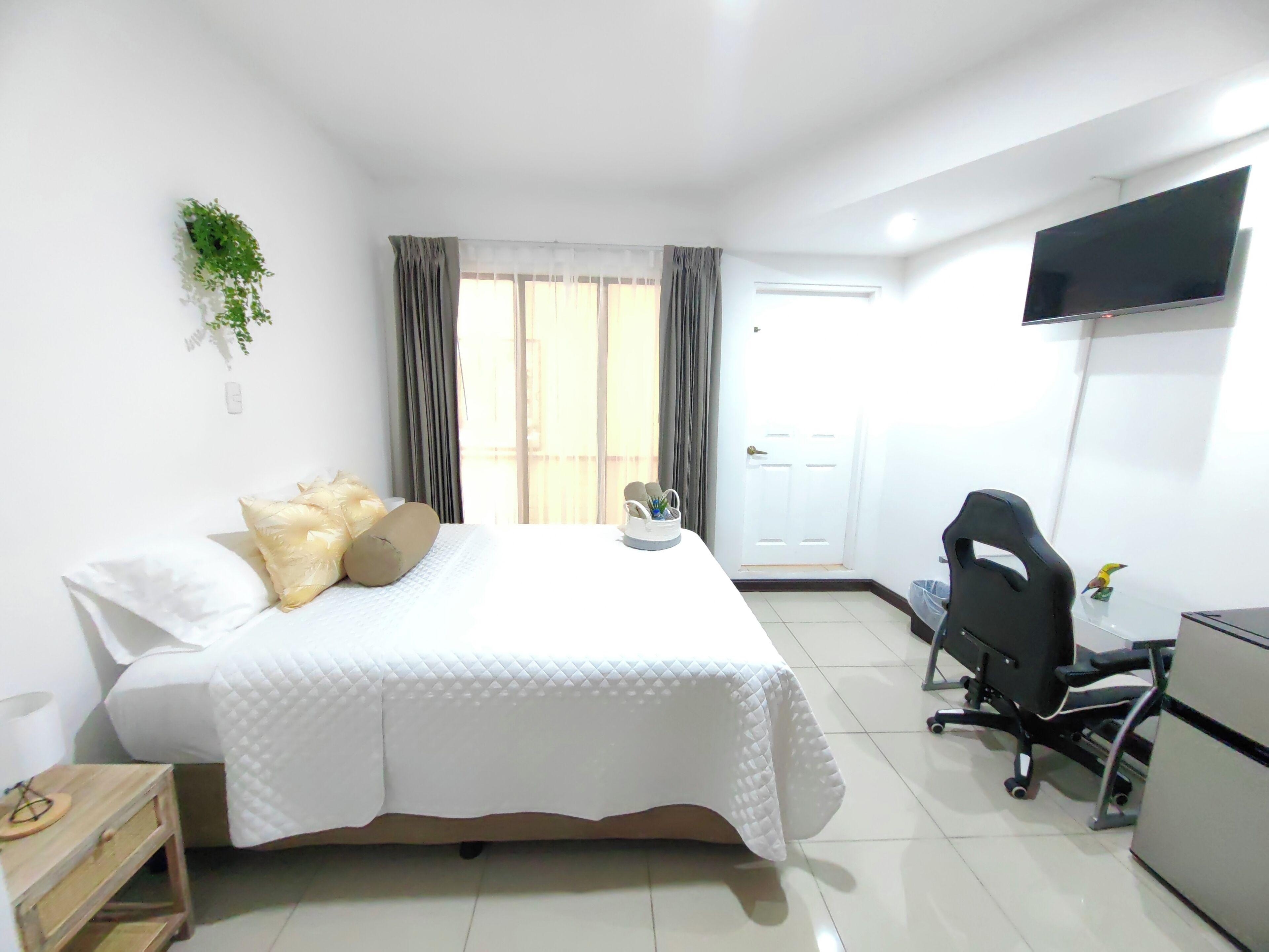 A hotel room with a bed, a desk, a chair, a TV, and a window with curtains.