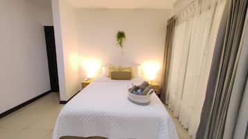 A neatly arranged hotel room with a large bed, bedside lamps, a small table with a plant, and a window with curtains.