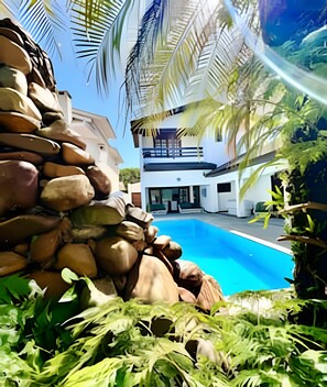 A modern house with a swimming pool, surrounded by greenery and rocks. - Casa com piscina em Acapulco Guarujá SP3 (Guarujá)