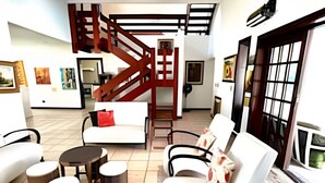 Amplia sala de estar con un sofá blanco, dos sillones, una mesa de centro y una escalera de madera.