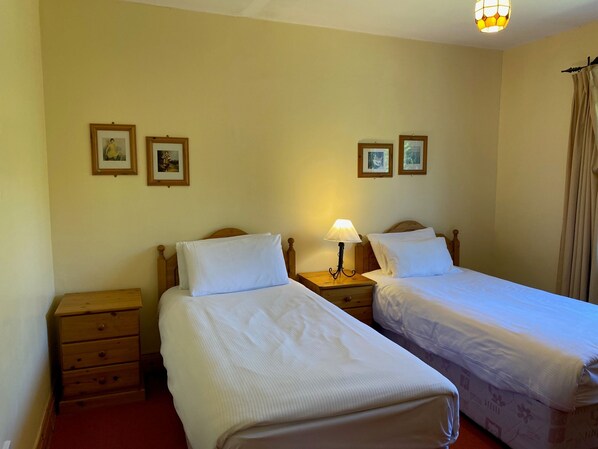 A room with two single beds, wooden nightstands, a lamp, and framed pictures on the wall. - Convenient Spacious 3 Bedroom Home in Kenmare Town (Kenmare)