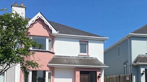 A two-story house with a pink and white facade, stone foundation, and a black door. - Convenient Spacious 3 Bedroom Home in Kenmare Town (Kenmare)