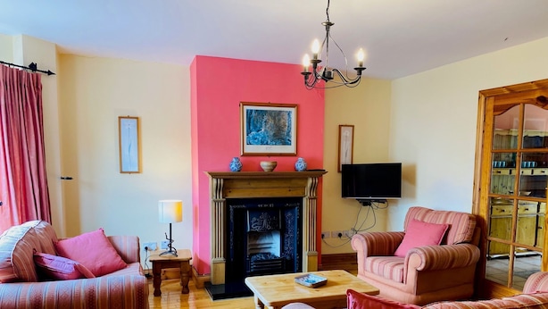 A living room with two sofas, a fireplace, a television, and a chandelier. - Convenient Spacious 3 Bedroom Home in Kenmare Town (Kenmare)