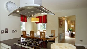 A modern kitchen with a gas stove, dining table, chairs, and a round wooden table.