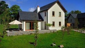 A modern two-story house with a stone foundation, a large patio with outdoor furniture, and a well-maintained lawn.
