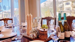 A dining table set with wine bottles, glasses, and decorative items, with a view of a mountain and buildings through the window.