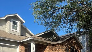 A two-story house with a brick exterior, a garage, and a front yard with a small garden and wooden posts. - Charming 3-bedroom house with AC, WiFi in pleasant San Antonio (San Antonio)