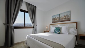A hotel room with a large bed, a nightstand, a window with curtains, and a painting on the wall.