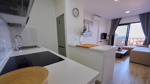 A modern kitchen with a sink, stove, and wooden bowl. A dining area with a table and chairs is visible.