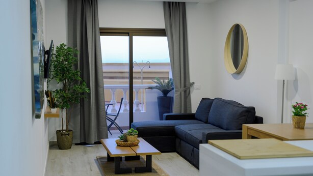 Un soggiorno moderno con divano, tavolino, pianta in vaso e vista su un balcone con ringhiera.