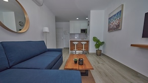 A modern living room with a blue sofa, a wooden coffee table, and a kitchen in the background.
