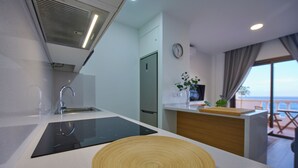 Een moderne keuken met een zwart inductiekookplaatje, een houten snijplank en uitzicht op het balkon.