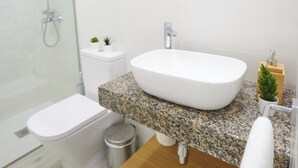 Een moderne badkamer met een wit wastafelmeubel, een granieten blad en een douchecabine met glazen wanden.