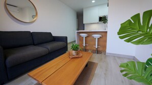 Een moderne woonkamer met een donkere bank, een houten salontafel en een ronde spiegel aan de muur.