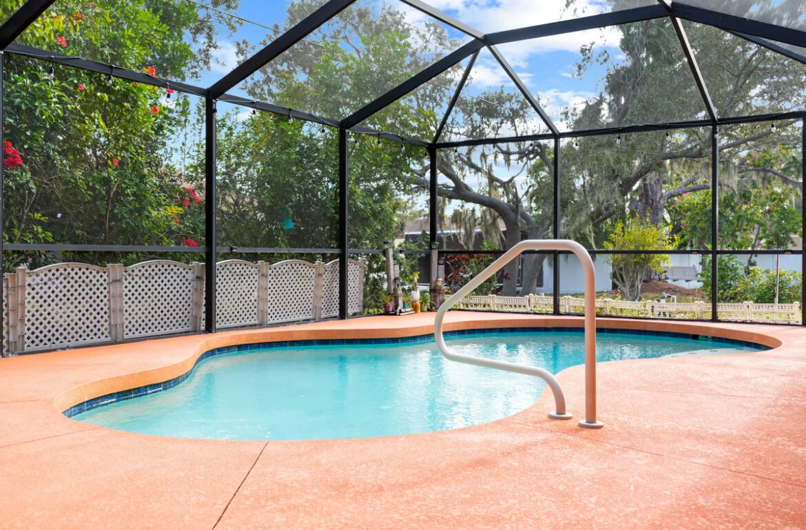 A covered swimming pool with a metal ladder, surrounded by a fence and trees.