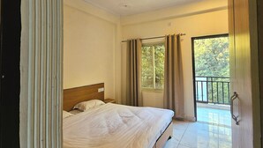 Una habitación de hotel con cama, ventilador de techo, ventana con cortinas y balcón.
