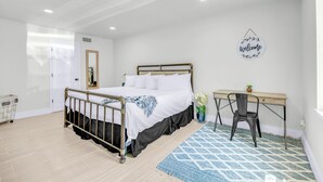 Un dormitorio con una cama, un escritorio, una silla, una planta pequeña y un letrero de bienvenida en la pared.