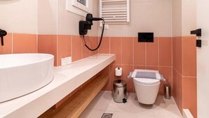A modern bathroom with a white sink, a toilet, and a hairdryer on the wall. - Mar25 #31 by Smart Cozy Suites (Athina)