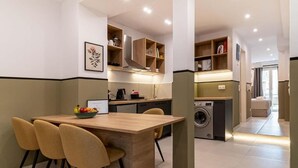 A modern kitchen with built-in appliances, a dining area with a table and chairs, and a laundry room. - Mar25 #31 by Smart Cozy Suites (Athina)