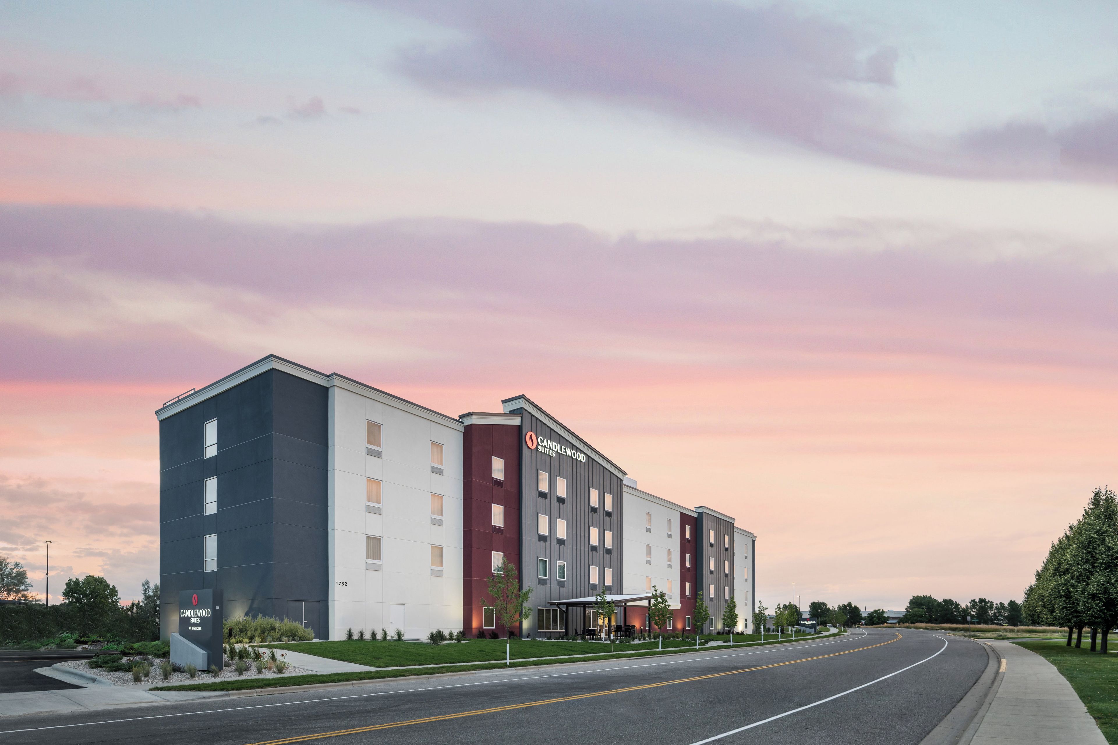 Un hôtel moderne, avec plusieurs étages et un toit plat, situé au bord d’une route, avec un ciel dégagé en arrière-plan.